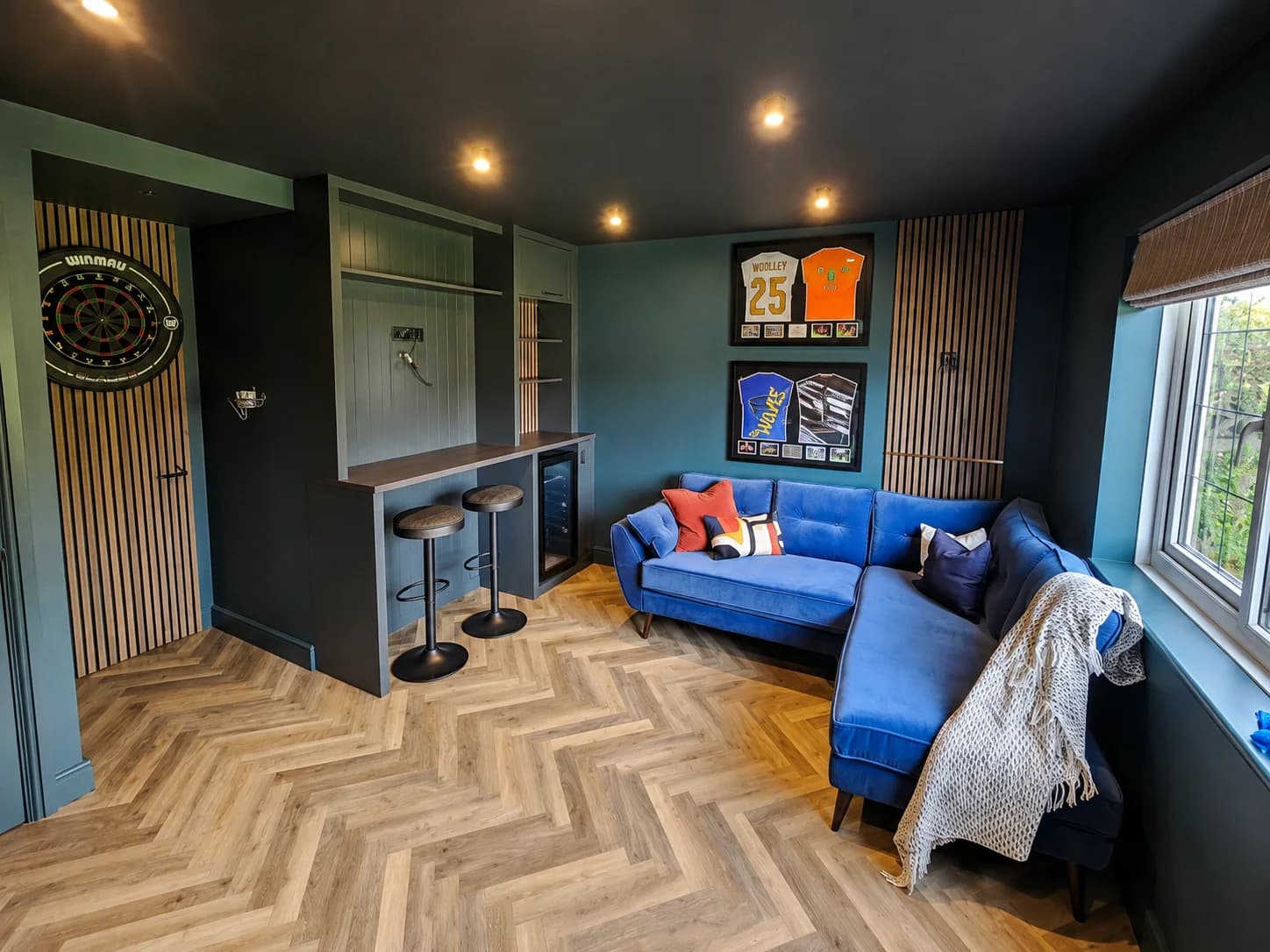 Dark entertainment room with fitted bar, slatted oak panelling and herringbone flooring