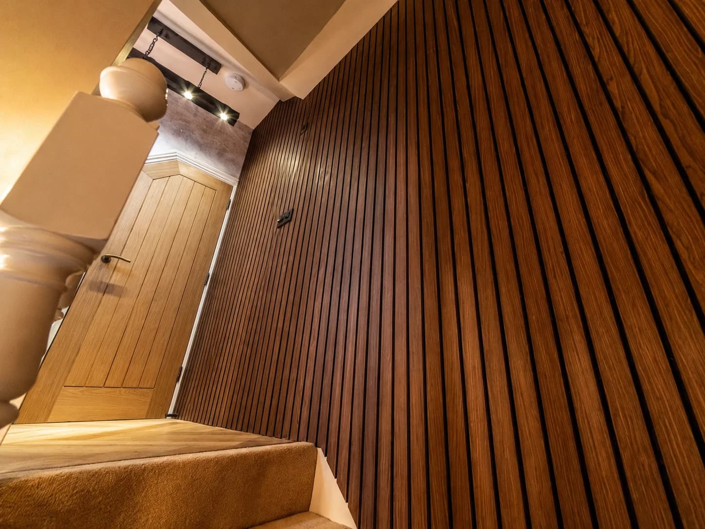 Floor-to-ceiling slatted oak panelling beside a staircase with an oak door