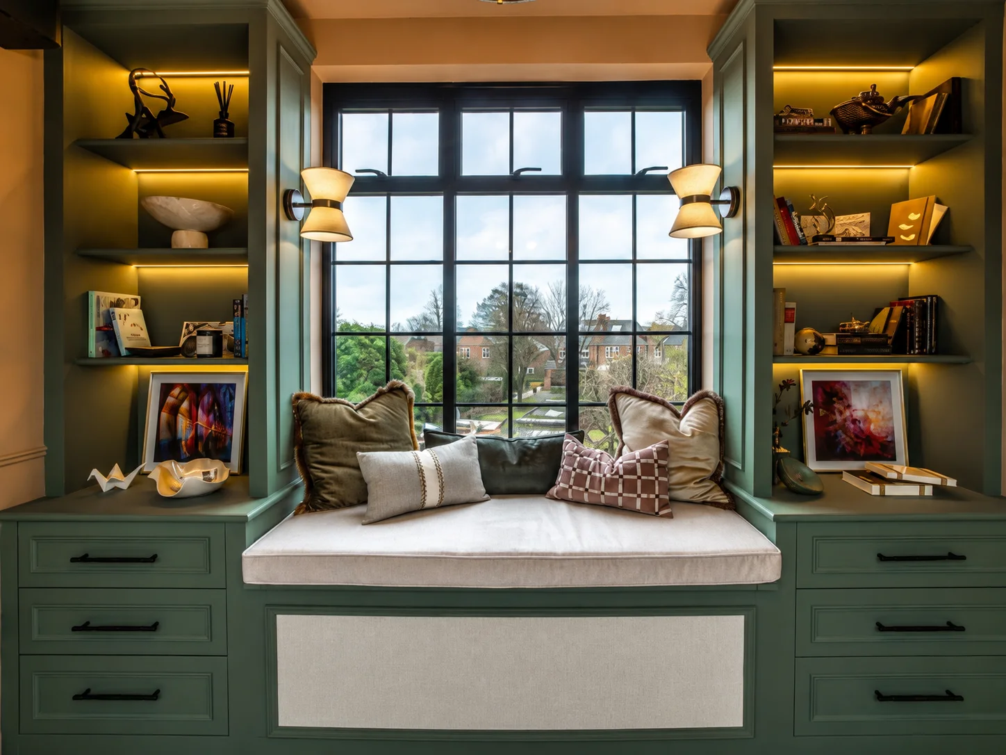 Bespoke green window seat with illuminated shelving and drawers built into a bedroom alcove